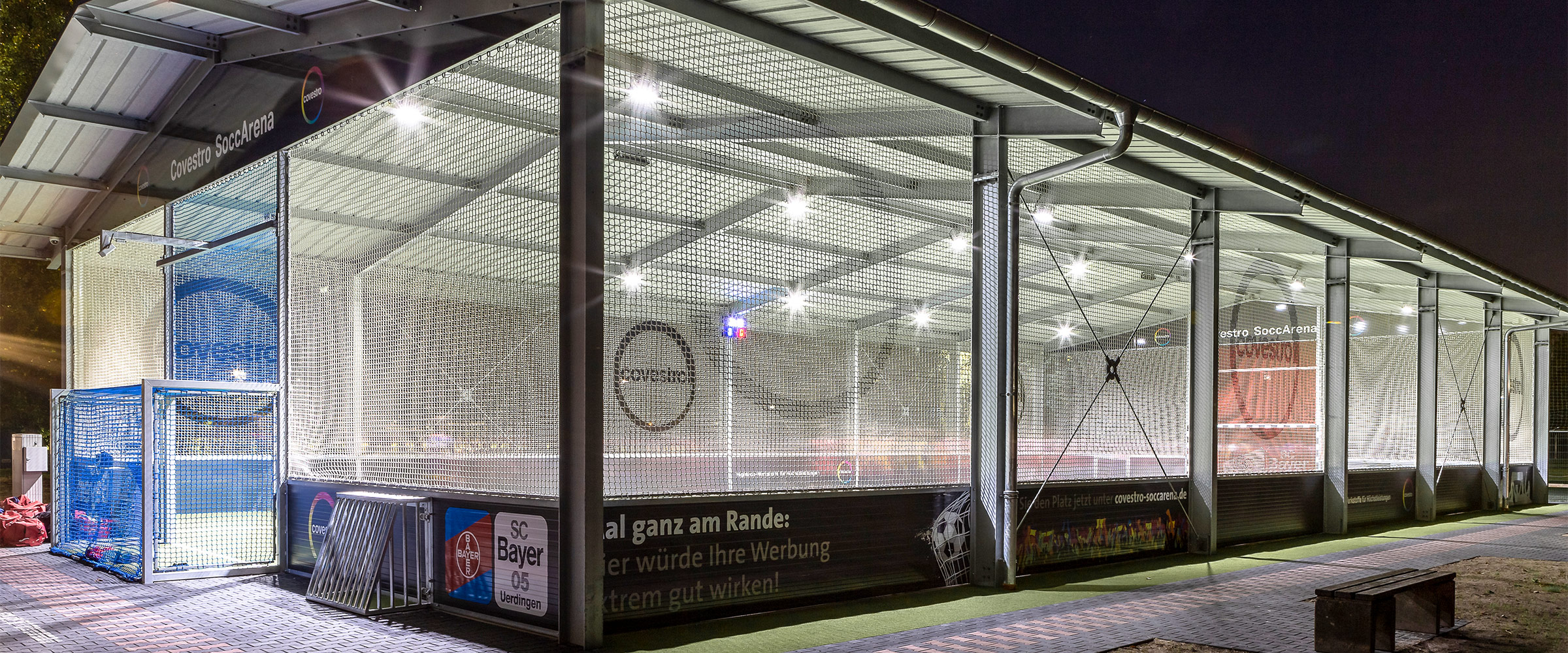 Die Cocestro SoccArena Soccerhalle Krefeld von außen. Helle LED Strahler beleuchten die moderne Soccerhalle bei Nacht.